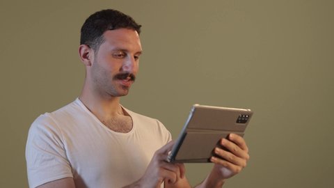 الدردشة مع الأهل والأصدقاء، استخدام تطبيقات وبرامج الأجهزة اللوحية، دمج التكنولوجيا والتقنيات الحديثة فى الحياه اليوميه ، رجل عربي خليجي سعودي يرتدي السروال والفانيله البيضاء  يحمل بيده جهاز التابلت، تصفح مواقع التواصل الاجتماعي