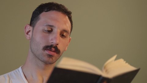 الاستمتاع بممارسة هواية المطالعة، الأنشطة الترفيهية المفيدة, رجل عربي خليجي سعودي يرتدي السروال والفانيله البيضاء يمسك بيده كتاب  ، الروايات والكتب التثقيفية