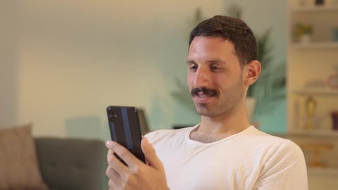 استخدام جهاز تقني حديث، الدردشة مع الأهل والأصدقاء،رجل عربي خليجي سعودي يرتدي السروال والفانيله البيضاء يمسك بيده الهاتف المحمول، دمج التقنية والتكنولوجيا بالحياة اليومية، تصفح مواقع التواصل الاجتماعي