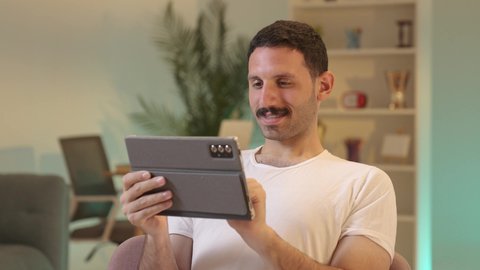 استخدام تطبيقات وبرامج الأجهزة اللوحية، الدردشة مع الأهل والأصدقاء، دمج التكنولوجيا والتقنيات الحديثة فى الحياه اليوميه ، رجل عربي خليجي سعودي يرتدي السروال والفانيله البيضاء  يحمل بيده جهاز التابلت، تصفح مواقع التواصل الاجتماعي