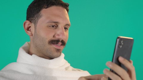 اجراء مكالمة هاتفية ، الدردشة مع الأهل والأصدقاء، استخدام جهاز تقني حديث، رجل عربي خليجي سعودي يرتدي لباس الاحرام يمسك بيده الهاتف المحمول، دمج التقنية والتكنولوجيا بالحياة اليومية، تصفح مواقع التواصل الاجتماعي