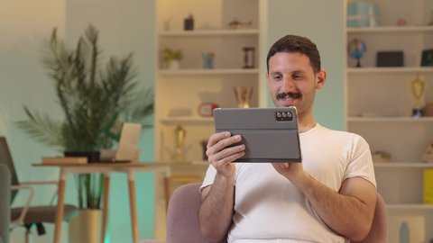 الدردشة مع الأهل والأصدقاء، استخدام تطبيقات وبرامج الأجهزة اللوحية،دمج التكنولوجيا والتقنيات الحديثة فى الحياه اليوميه ، رجل عربي خليجي سعودي يرتدي السروال والفانيله البيضاء  يحمل بيده جهاز التابلت، تصفح مواقع التواصل الاجتماعي