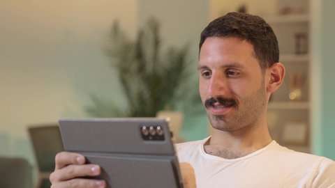 استخدام تطبيقات وبرامج الأجهزة اللوحية، الدردشة مع الأهل والأصدقاء، دمج التكنولوجيا والتقنيات الحديثة فى الحياه اليوميه ، رجل عربي خليجي سعودي يرتدي السروال والفانيله البيضاء  يحمل بيده جهاز التابلت، تصفح مواقع التواصل الاجتماعي