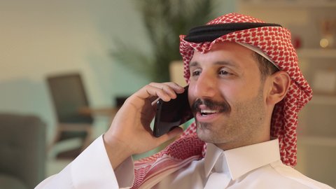 Integrating technology and technology into daily life, making a phone call, chatting with family and friends, using a modern technical device, an Arab Gulf Saudi man wearing traditional attire and a ghutrah holding a mobile phone, browsing social media sites.