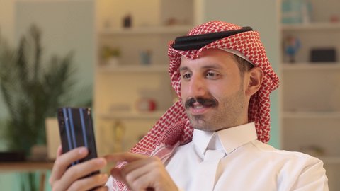 الدردشة مع الأهل والأصدقاء، اجراء مكالمة هاتفية ، استخدام جهاز تقني حديث، رجل عربي خليجي سعودي يرتدي الزى التقليدي والشماغ  يمسك بيده الهاتف المحمول، دمج التقنية والتكنولوجيا بالحياة اليومية، تصفح مواقع التواصل الاجتماعي