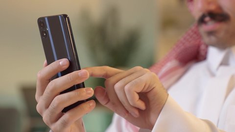 استخدام جهاز تقني حديث، اجراء مكالمة هاتفية ، الدردشة مع الأهل والأصدقاء، رجل عربي خليجي سعودي يرتدي الزى التقليدي والشماغ  يمسك بيده الهاتف المحمول، دمج التقنية والتكنولوجيا بالحياة اليومية، تصفح مواقع التواصل الاجتماعي