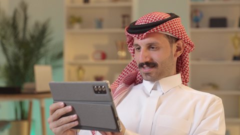 استخدام تطبيقات وبرامج الأجهزة اللوحية، الدردشة مع الأهل والأصدقاء، دمج التكنولوجيا والتقنيات الحديثة فى الحياه اليوميه ، رجل عربي خليجي سعودي يرتدي الزى التقليدي والشماغ يحمل بيده جهاز التابلت، تصفح مواقع التواصل الاجتماعي