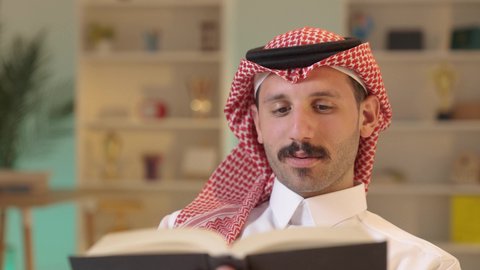 الاستمتاع بممارسة هواية المطالعة، الأنشطة الترفيهية المفيدة,رجل عربي خليجي سعودي يرتدي الزى التقليدي والشماغ يجلس على كرسي مريح يقوم بقراءة القصص ، الروايات والكتب التثقيفية