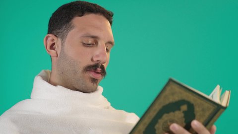 رجل عربي خليجي سعودي يرتدي لباس الاحرام يقرأ من المصحف الشريف، التمعن بسور القرآن الكريم, مفهوم العبادة والطاعة والتقرب الى الله في شهر رمضان المبارك, تدبر الآيات القرآنية والتفكر بها،خلفية خضراء ، كروما