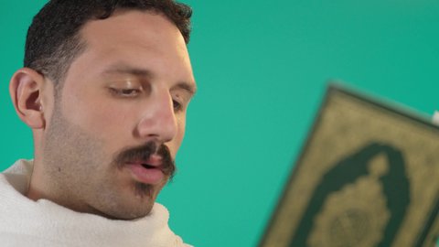 التمعن بسور القرآن الكريم, مفهوم العبادة والطاعة والتقرب الى الله في شهر رمضان المبارك, تدبر الآيات القرآنية والتفكر بها، رجل عربي خليجي سعودي يرتدي لباس الاحرام يقرأ من المصحف الشريف، خلفية خضراء ، كروما