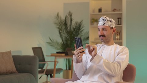 دمج التقنية والتكنولوجيا بالحياة اليومية،الدردشة مع الأهل والأصدقاء، استخدام جهاز تقني حديث، رجل عربي خليجي عماني يرتدي الدشداشة والكمة يمسك بيده الهاتف المحمول،  تصفح مواقع التواصل الاجتماعي