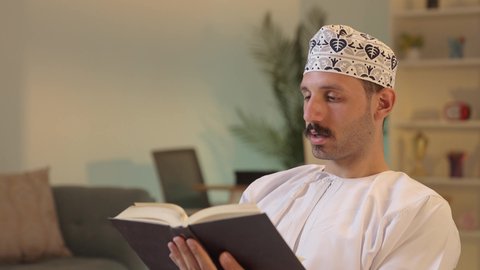 الاستمتاع بممارسة هواية المطالعة، الأنشطة الترفيهية المفيدة, رجل عربي خليجي عماني يرتدي الدشداشة والكمه العمانية يجلس على كرسي مريح يقوم بقراءة القصص ، الروايات والكتب التثقيفية