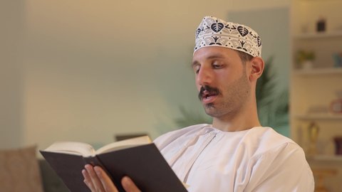 الأنشطة الترفيهية المفيدة, الاستمتاع بممارسة هواية المطالعة، رجل عربي خليجي عماني يرتدي الدشداشة والكمه العمانية يجلس على كرسي مريح يقوم بقراءة القصص ، الروايات والكتب التثقيفية
