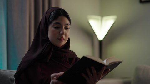 الروايات والكتب التثقيفية، الأنشطة الترفيهية المفيدة, الاستمتاع بممارسة هواية المطالعة، امراه عربيه خليجيه عمانيه ترتدي العباءه والحجاب  تجلس فى غرفه المعيشة تقوم بقراءة القصص