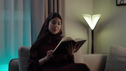 الأنشطة الترفيهية المفيدة, الاستمتاع بممارسة هواية المطالعة، امراه عربيه خليجيه عمانيه ترتدي العباءه والحجاب  تجلس فى غرفه المعيشة تقوم بقراءة القصص ، الروايات والكتب التثقيفية