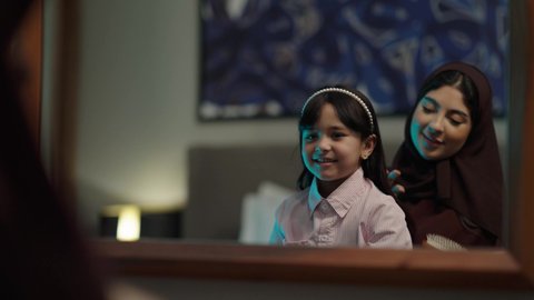 ايماءات السرور والسعاده، الحب والاعتناء بالابناء ،الاناقه والاعتناء بالمظهر الخارجي، أم عربية خليجية عمانيه ترتدي العباءه والحجاب تقوم بتصفيف شعر ابنتها، ارتداء الأزياء التقليدية ، العناية بمظهر الشعر والنظافة الشخصية