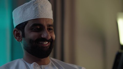 استخدام تطبيقات وبرامج الأجهزة اللوحية، الدردشة مع الأهل والأصدقاء، دمج التكنولوجيا والتقنيات الحديثة فى الحياه اليوميه ، رجل عربي خليجي عماني يرتدي الدشداشة والكمة يحمل بيده جهاز التابلت فى غرفه المعيشة ، تصفح مواقع التواصل الاجتماعي