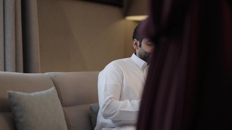 مناقشة الأفكار وتبادل الآراء، ايماءات السعادة و السرور، امراه عربيه خليجيه سعودية محجبة ترتدي العباءة و الحجاب تجلس فى غرفه المعيشة برفقة زوجها تحمل جهاز التابلت ، قضاء أوقات الفراغ بالتثقيف والتعلم, تنمية مهارات القراءة