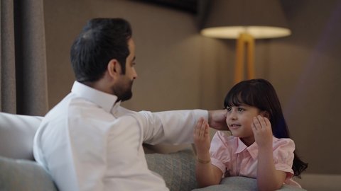 الاستمتاع بالأجواء العائليه السعيده في أيام العطله، نقاشات وحوارات الأباء مع الأبناء، اب عربي خليجي سعودي يرتدي الثوب الابيض يجلس بغرفه المعيشه وتتبادل أطراف الأحاديث مع ابنته، مفهوم العائله السعوديه المترابطه، بناء علاقات أسريه قويه