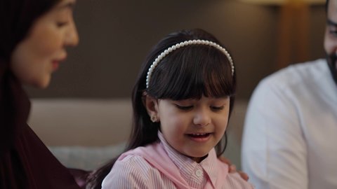 أجواء أسرية مليئة بالمودة، عائلة سعودية تقضي وقت ممتع، مفهوم الأسرة السعيدة المترابطة، رجل عربي خليجي سعودي يرتدي الثوب الابيض يجلس فى غرفة المعيشة مع زوجته و ابنته، تبادل الحوار والنقاش المسلي، الرعاية والاهتمام بالأبناء, ايماءات السعادة و السرور