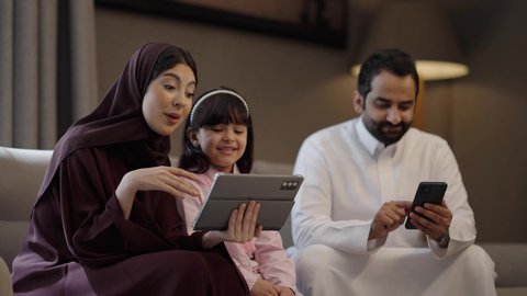 Expressions of agreement and acceptance, browsing social media on mobile, talking and communicating with family and friends, making video calls over the internet, using modern technological devices, a Saudi Gulf Arab family sitting in the living room using a tablet, expressions of happiness and joy.