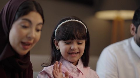 إيماءة ترحيبية برفع اليد ، التحدث والتواصل مع العائلة والأصدقاء، إجراء مكالمات الفيديو عبر الانترنت، استخدام اجهزة تقنية حديثة، عائلة عربيه خليجيه سعودية تجلس فى غرفه المعيشة تستخدم جهاز التابلت، تعابير السعادة و السرور