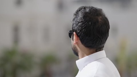تصوير مقرب لرجل عربي خليجي سعودي مبتسم يرتدي الثوب الابيض والنظارة الشمسية ينظر الى الكاميرا بإيماءات السرور، استخدام العدسات الطبية الملونة لحماية العين من أشعة الشمس، الاهتمام بالأناقة والمظهر الخارجي، مفهوم الرجولة والثقة بالنفس
