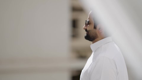 الاهتمام بالأناقة والمظهر الخارجي، مفهوم الرجولة والثقة بالنفس، تصوير مقرب لرجل عربي خليجي سعودي مبتسم يرتدي الثوب الابيض والنظارة الشمسية ينظر الى الكاميرا بإيماءات السرور، استخدام العدسات الطبية الملونة لحماية العين من أشعة الشمس