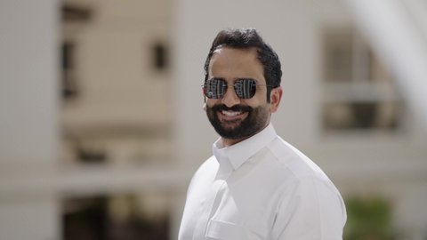 مفهوم الرجولة والثقة بالنفس، الاهتمام بالأناقة والمظهر الخارجي، تصوير مقرب لرجل عربي خليجي سعودي مبتسم يرتدي الثوب الابيض والنظارة الشمسية ينظر الى الكاميرا بإيماءات السرور، استخدام العدسات الطبية الملونة لحماية العين من أشعة الشمس