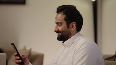 مفهوم الأمان والإستقرار العائلي، تصفح الانترنت ومواقع التواصل الاجتماعي عبر الجوال، تبادل الاحاديث والاخبار بين افراد العائلة، المحافظة على الترابط الأسري، امراه عربيه خليجيه سعودية ترتدي العباءة و الحجاب تجلس فى غرفه المعيشة برفقة زوجها تستخدم الحاسب المحمول