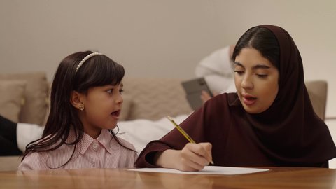 مراجعة الدروس اليومية, مفهوم العودة إلى المدارس، التعليم في المملكة العربية السعودية, الاستعداد للعام الدراسي الجديد,فتاة عربية خليجية سعودية ترتدي الزي الكاجوال تجلس فى غرفة المعيشة برفقة والدتها,  اهتمام الآباء بالأبناء