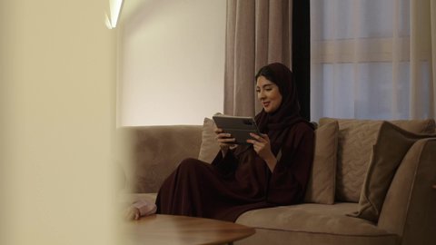 قضاء وقت ممتع، تنمية وتطوير مهارات الكتابة، الاجتهاد والاستعداد للإختبارات المدرسية، بنت عربيه خليجيه سعودية تقوم بحل الواجبات المدرسية ، امراه عربيه خليجيه سعودي ترتدي العباءة و الحجاب تجلس على الاريكة تمسك بيديها جهاز التابلت