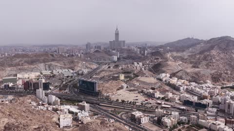 التشكيل والتكوين الصخري للمرتفع الجبلي في مكة المكرمة، الأفق والأبراج وناطحات السحاب في وقت النهار، تصوير درون جوي لحركة سير السيارات على ممر جبلي ملتوي، الأجواء الضبابية على الجبل في المملكة العربية السعودية،  الفن الهندسي المعماري لمعالم دينية إسلامية مقدسة