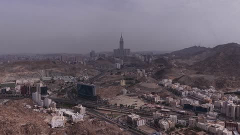 التشكيل والتكوين الصخري للمرتفع الجبلي في مكة المكرمة، الأجواء الضبابية على الجبل في المملكة العربية السعودية، طريق عقبة الهدا في مدينة الطائف، تصوير درون جوي لحركة سير السيارات على ممر جبلي ملتوي، خلفية برج الساعة في منطقة الحرم