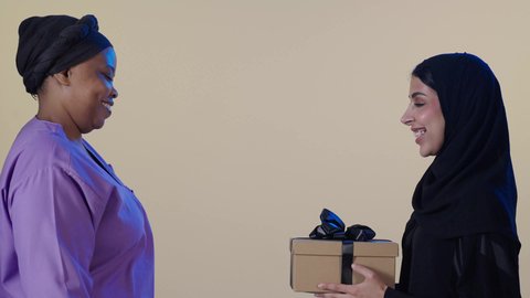 مهن ووظائف نسائية، الإحسان في التعامل مع الخادمات في البيوت في السعودية، أجواء عائلية سعيدة مليئة بالتقدير والاحترام، امراه عربيه خليجيه سعودية ترتدي العباءة و الحجاب تقوم بتقديم علبة هدية لخادمة فلبينية لجودة خدمتها وأدائها