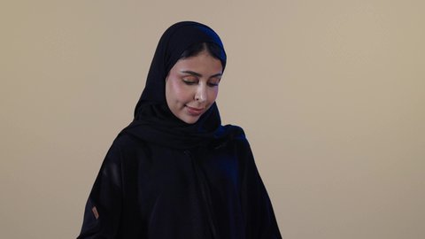 مفهوم التدبير المنزلي، إتمام المهام الروتينية،  استخدام الجهاز الكهربائي، تجفيف وتنظيم الملابس، بورتريه لامراة عربيه خليجيه سعودية ترتدي عباءة سوداء تقوم بكي الملابس باستخدام المكواة، خلفية بنية