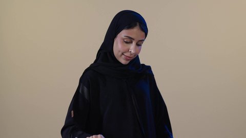 إتمام المهام الروتينية، مفهوم التدبير المنزلي،  استخدام الجهاز الكهربائي، تجفيف وتنظيم الملابس، بورتريه لامراة عربيه خليجيه سعودية ترتدي عباءة سوداء تقوم بكي الملابس باستخدام المكواة، خلفية بنية