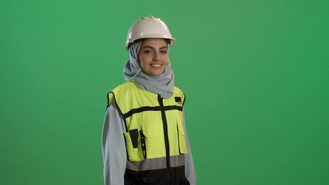 تحقيق حلم النجاح والوصول لمهنة الهندسة بتعابير الفخر، المشاريع الهندسية ومخططات الإعمار, بورتريه مقرب لفتاة عربية خليجية سعودية مبتسمة ترتدي سترة الحماية والخوذة وتنظر إلى الكاميرا بايماءات السعادة والسرور, العمل في القطاع الهندسي، خلفية خضراء, كروما