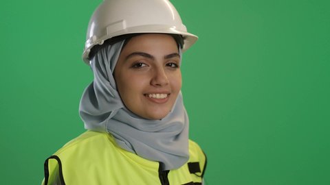 المشاريع الهندسية ومخططات الإعمار, تحقيق حلم النجاح والوصول لمهنة الهندسة بتعابير لفخر, بورتريه مقرب لفتاة عربية خليجية سعودية مبتسمة ترتدي سترة الحماية والخوذة وتنظر إلى الكاميرا بايماءات السعادة والسرور, العمل في القطاع الهندسي، خلفية خضراء, كروما