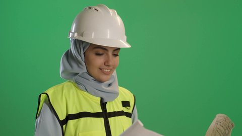 chroma,Architectural design and plan review; a close-up portrait of a veiled Saudi Arabian Gulf female engineer wearing a protective vest and helmet, holding a construction plan; engineering project management; women's careers and jobs; green screen background