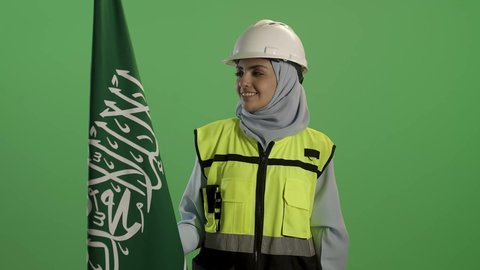 اليوم الوطني السعودي 23 سبتمبر, بورتريه لمهندسة عربية خليجية سعودية ترتدي سترة الحماية والخوذة,  تمسك علم المملكة بإيماءات الفخر, يوم العلم 11 مارس, خلفية خضراء, كروما