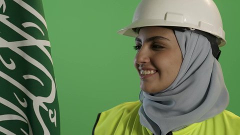 الاحتفال بالأعياد الوطنية, اليوم الوطني السعودي 23 سبتمبر, بورتريه مقرب لمهندسة عربية خليجية سعودية ترتدي سترة الحماية والخوذة,  تمسك علم المملكة بإيماءات الفخر, يوم العلم 11 مارس, خلفية خضراء, كروما