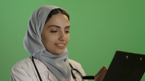 تدوين المعلومات والملاحظات الطبية, بورتريه لطبيبة عربية خليجية سعودية محجبة ترتدي المعطف الأبيض و السماعة, الاهتمام بالمرضى والتشخيص العلاجي لهم ,  مهن ووظائف نسائية,  خلفية خضراء, كروما