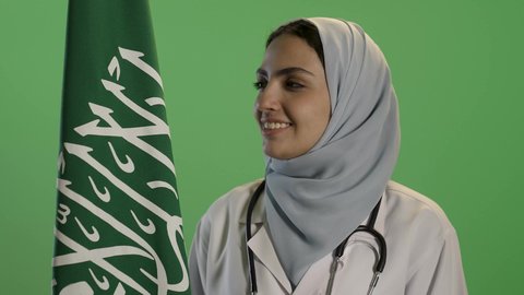 ذكرى تأسيس الدولة السعودية الأولى 22 فبراير, بورتريه لطبيبة عربية خليجية سعودية ترتدي الحجاب مع المعطف الابيض, النظرالى علم المملكة بإيماءات الفخر, التباهي بإنجازات البلاد, خلفية خضراء, كروما