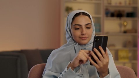 التواصل والاطمئنان عن الأهل والأصدقاء, امرأة عربية خليجية سعودية ترتدي العباءة الرمادية والحجاب تقوم بإستخدام الهاتف المحمول, مشاركة اللحظات السعيدة على وسائل التواصل الاجتماعي, قضاء وقت ممتع عبر الجوال مع الأصحاب