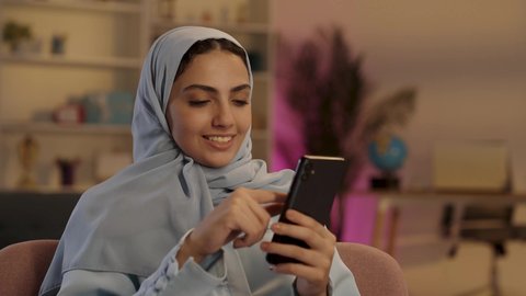 التقنيات المتطورة والتكنولوجيا الحديثة, امرأة عربية خليجية سعودية ترتدي العباءة الرمادية والحجاب تقوم بإستخدام الهاتف المحمول, مشاركة اللحظات السعيدة على وسائل التواصل الاجتماعي, قضاء وقت ممتع عبر الجوال مع الأصحاب