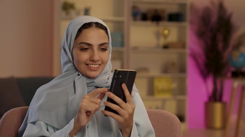 A veiled Saudi Arabian woman from the Gulf region, wearing a gray abaya, is browsing social media and using a mobile phone, demonstrating the use of modern technology.