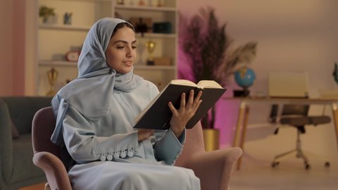 توسيع المعرفة وتعزيز الثقافة الفكرية, امرأة عربية خليجية سعودية ترتدي العباءة الرمادية والحجاب تحمل بيدها كتاب تثقيفي، الاستمتاع بقراءة الروايات والقصص , إيماءات التركيز والاندماج