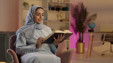 امرأة عربية خليجية سعودية ترتدي العباءة الرملدية والحجاب تحمل بيدها كتاب تثقيفي، الاستمتاع بقراءة الروايات والقصص , إيماءات التركيز والاندماج