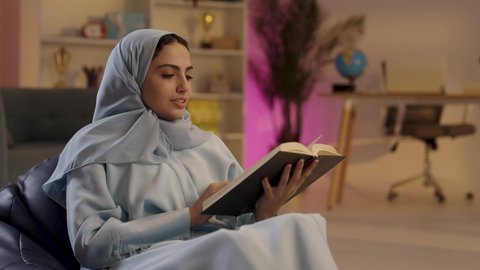 هواية المطالعة والاستكشاف, امرأة عربية خليجية سعودية ترتدي العباءة الرمادية والحجاب تحمل بيدها كتاب تثقيفي، الاستمتاع بقراءة الروايات والقصص , إيماءات التركيز والاندماج